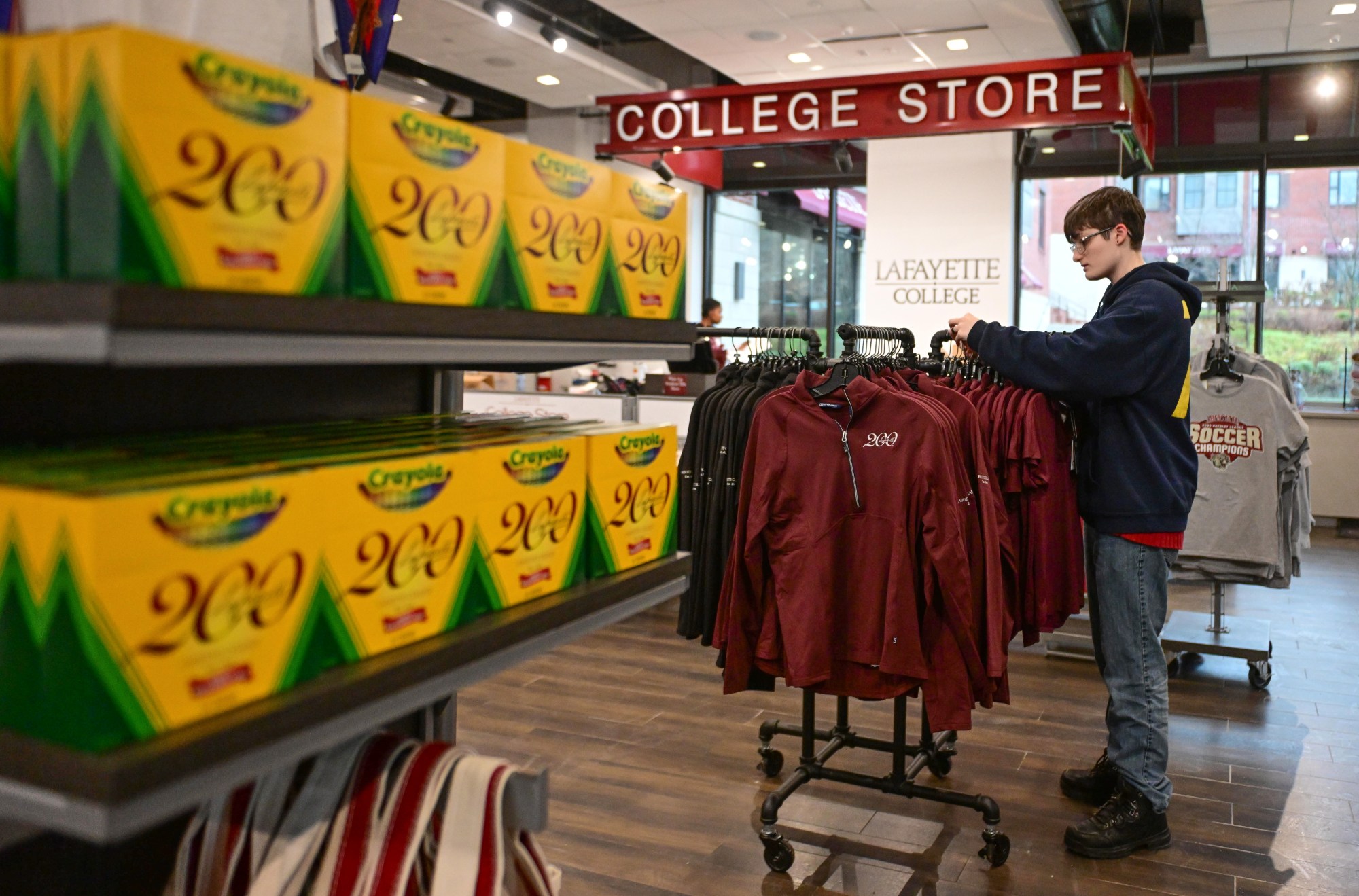 Matt Germs arranges merchandise Friday, Dec. 19, 2025, at the Lafayette College store in Easton. To mark its bicentennial in 2026 the school is offering themed merchandise such as clothing from Abercrombie & Fitch, special colors from Crayola and Burpee seeds for the Marquis Marigold flowers. (Monica Cabrera/The Morning Call)
