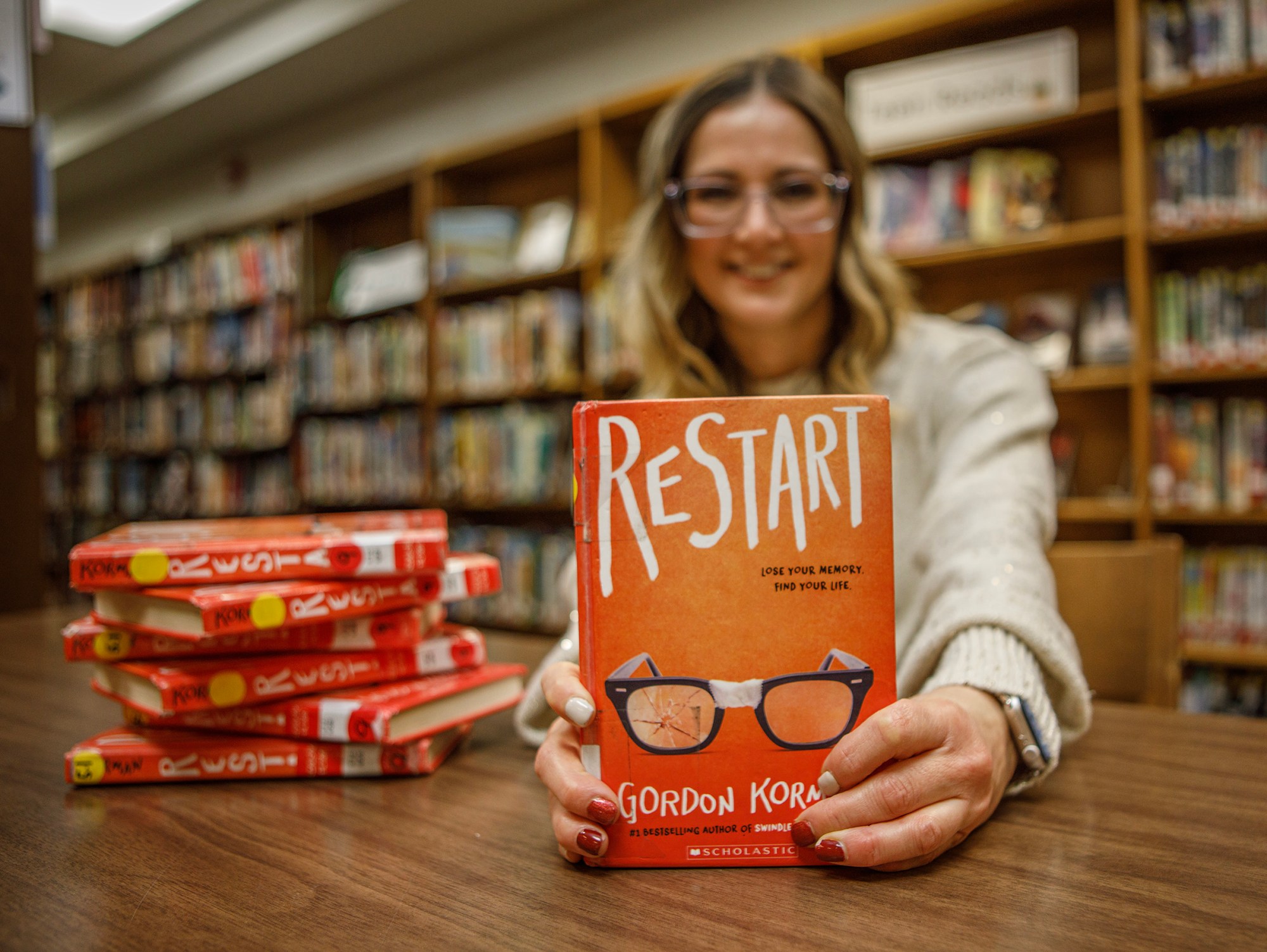 Kelly Flynn, librarian at Orefield Middle School, poses with a copy of “Restart” by Gordon Korman on Thursday, Dec. 18, 2025, at the school in South Whitehall Township. Korman’s book is one of Flynn’s book recommendations for middle-school readers. (Jane Therese/Special to The Morning Call)
